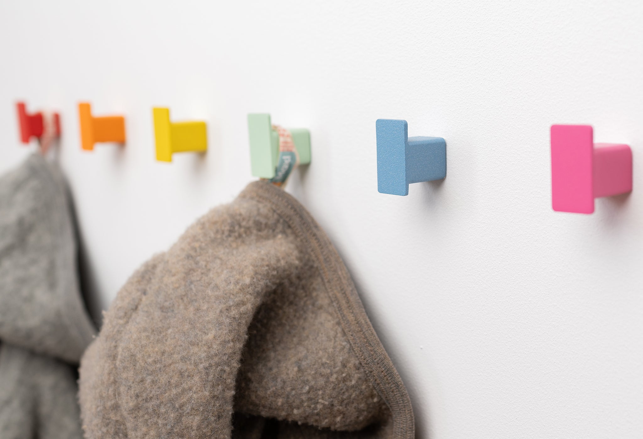 Kindergarderobe CAPRI von SAM Exclusive Interior im Close UP. Zwei Kinderjacken hängen an zwei bunten Haken. Schräg fotografiert.
