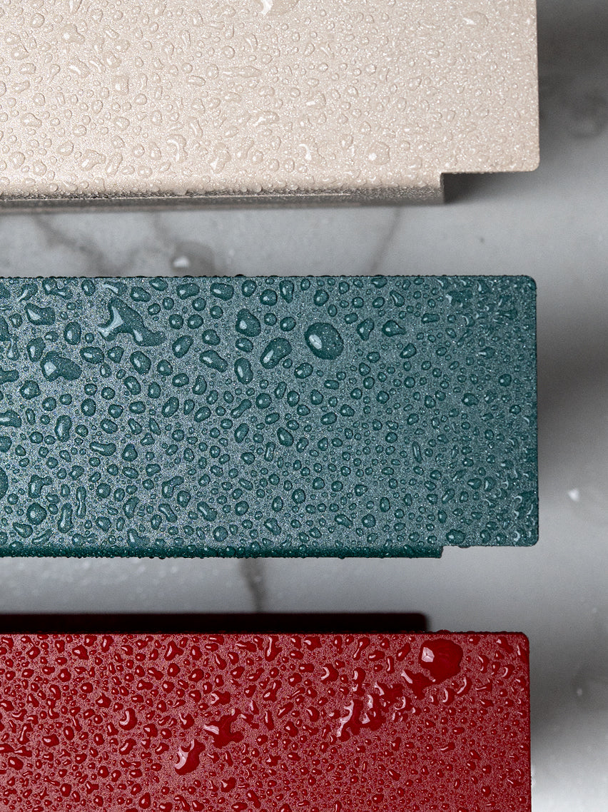 Close Up von pulverbeschichteten Duschregalen in den Farben Champagner, Sparkling Green und Velvet Red. Wassertropfen perlen auf der wasserfesten pulverbeschichteten Metalloberfläche ab.