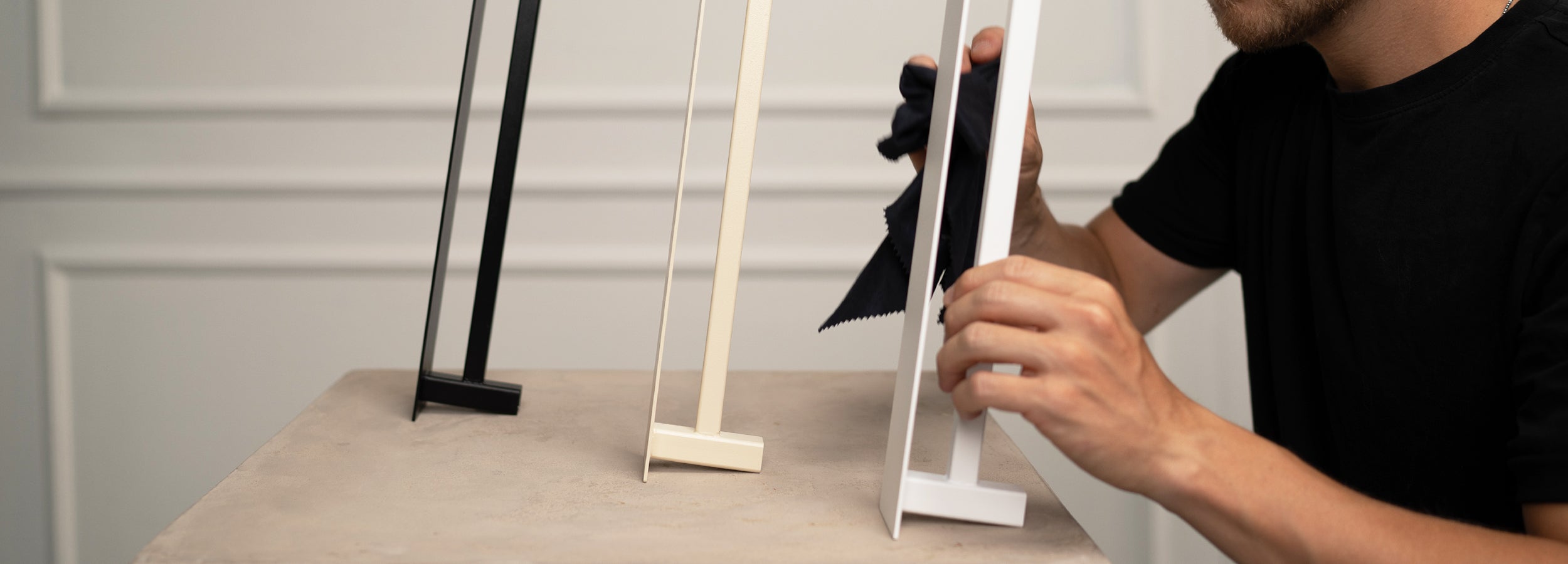 Hände mit Microfasertuch reinigen einen Handuchhalter in weiß im Hintergrund stehen weitere Handtuchhalter in beige und schwarz