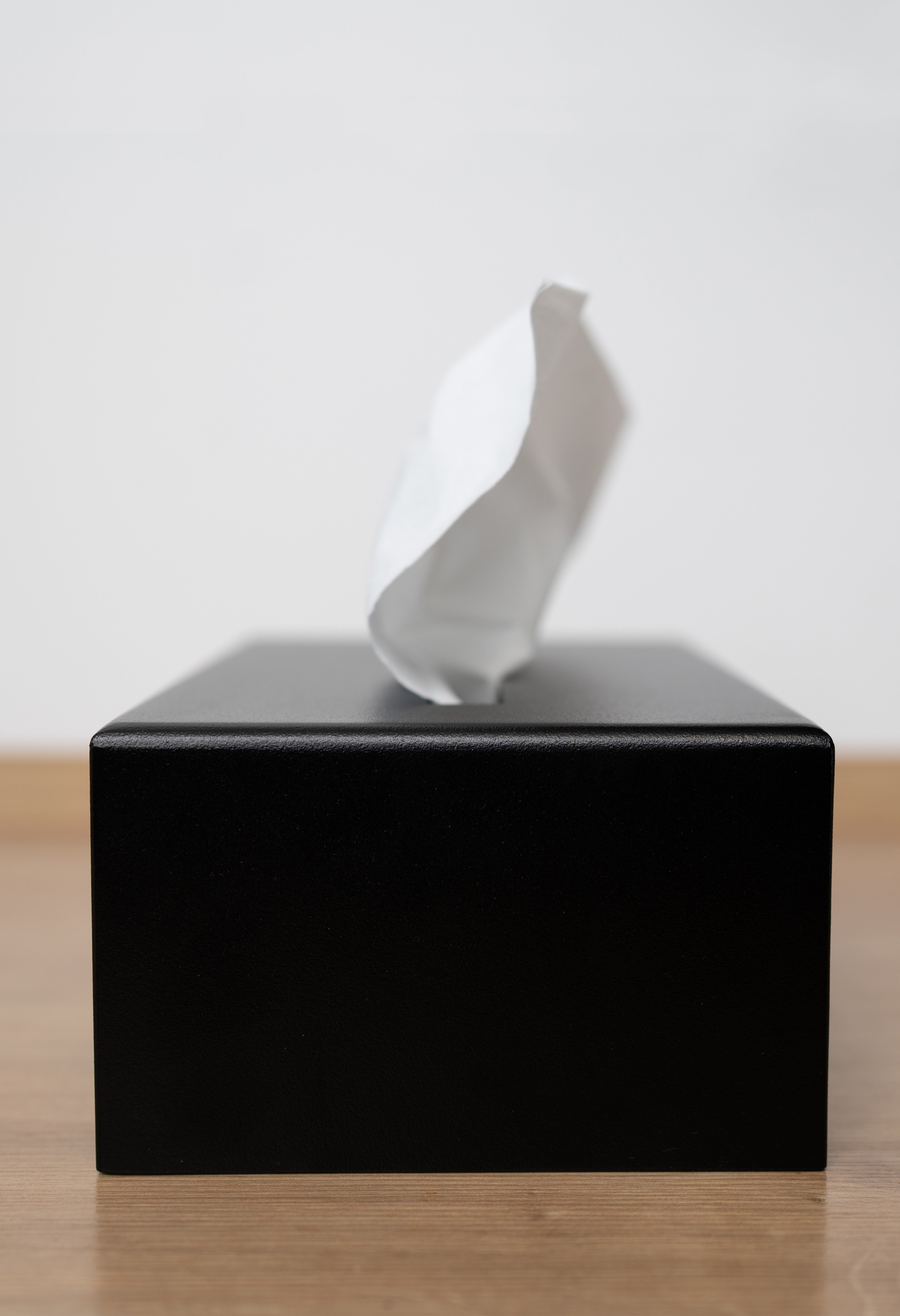 Kosmetiktuchbox in schwarz auf in Seitenansicht Close Up auf einem hellen Holzuntergrund.