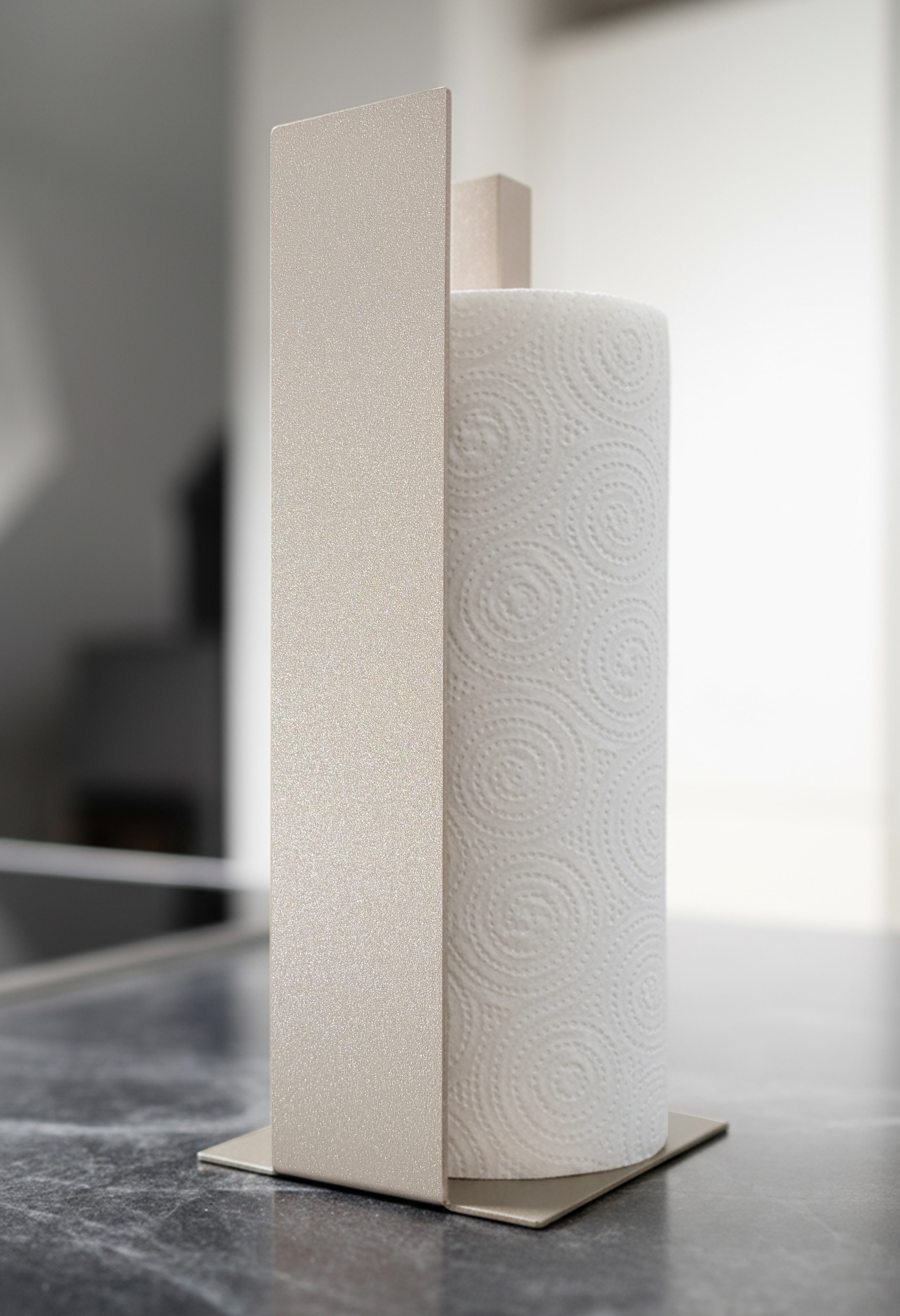 Küchenrollenhalter Granada pulverbeschichtet in Champagner, glitzernd, metallic, auf einer dunklen Marmorarbeitsfläche in einer hellen Küche. Schräge Ansicht.