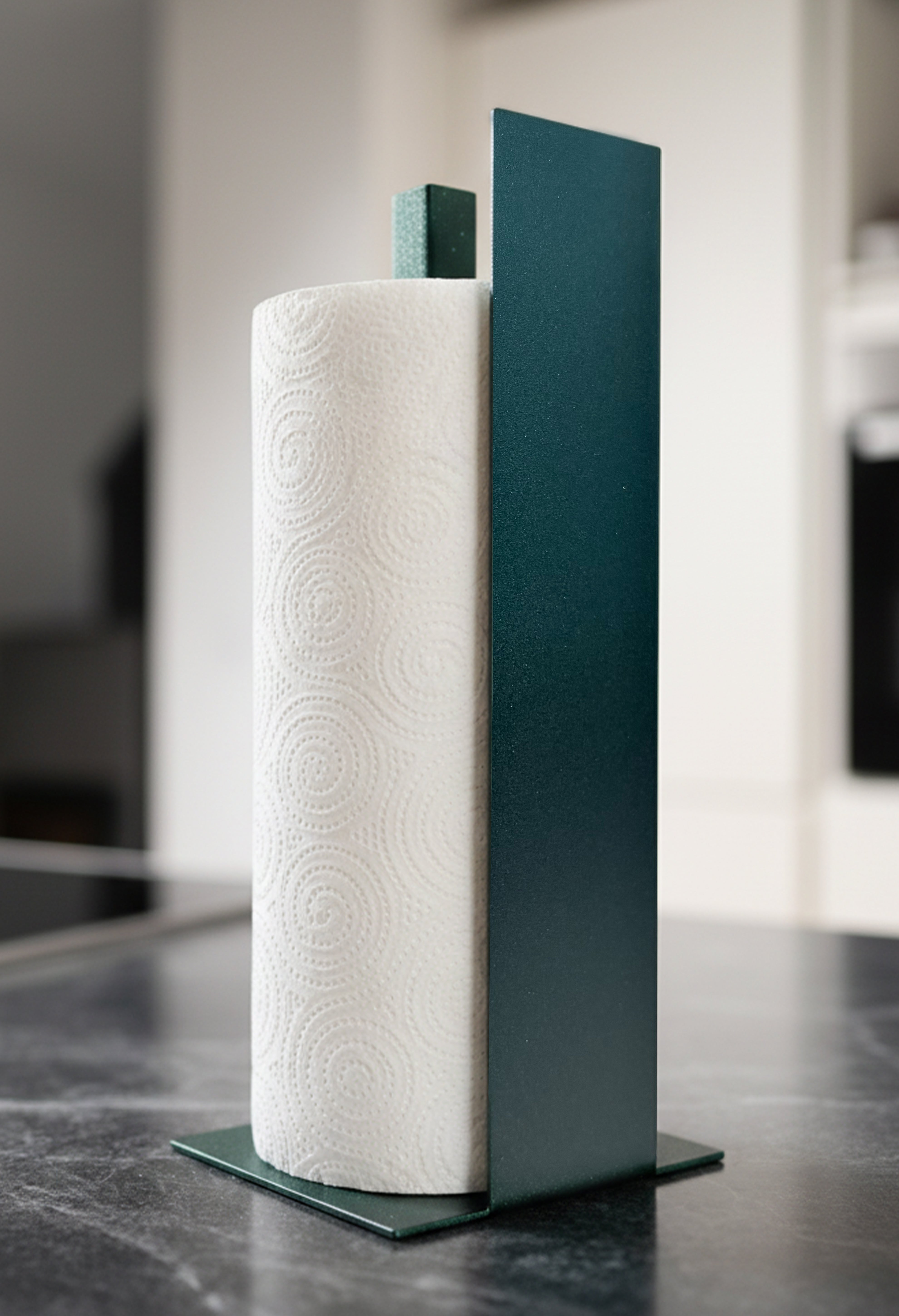 Küchenrollenhalter Granada pulverbeschichtet in Sparkling Green, glitzernd, metallic, auf einer dunklen Marmorarbeitsfläche in einer hellen Küche. Schräge Ansicht von vorne.