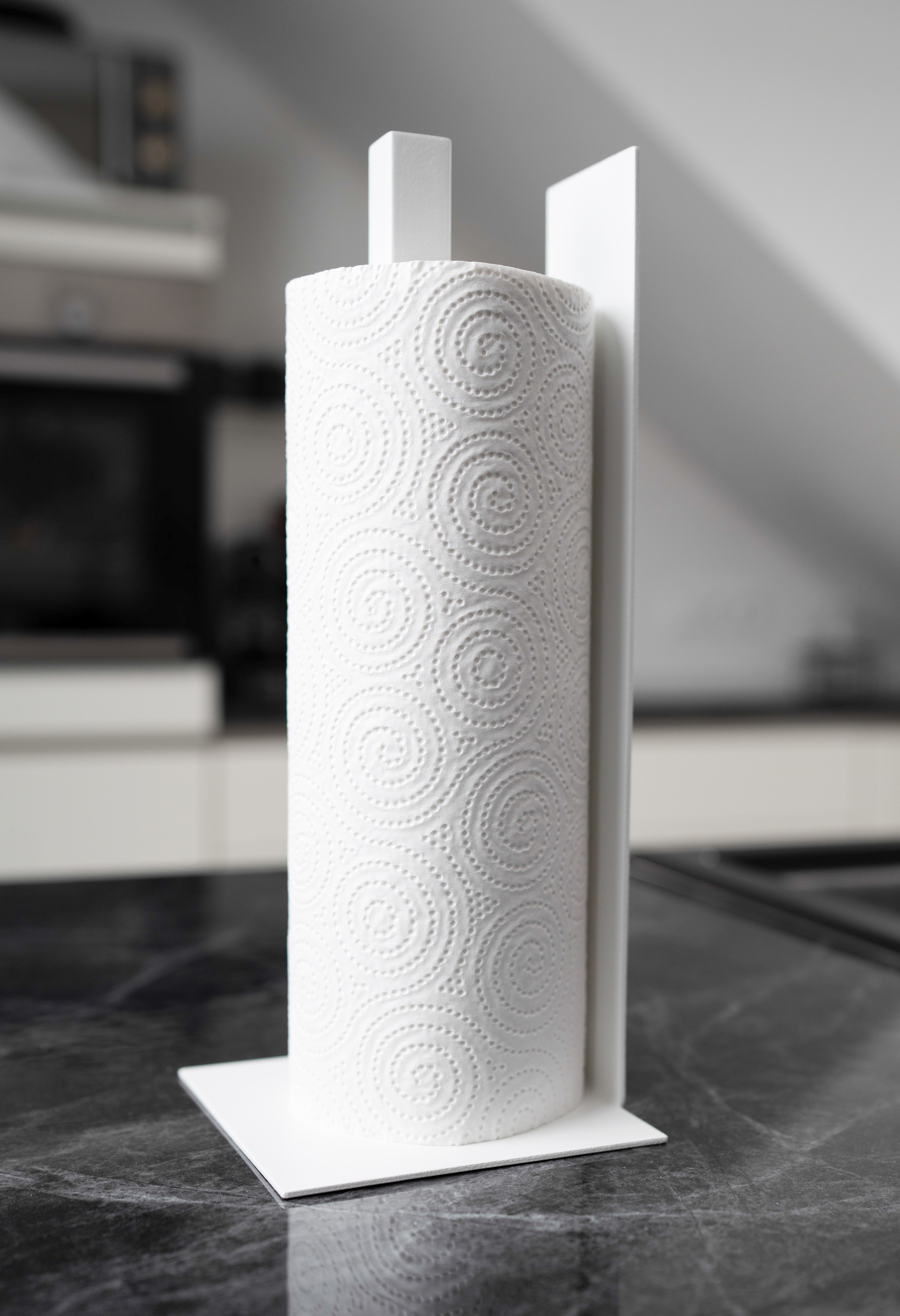 Küchenrollenhalter Granada pulverbeschichtet in matt weiss auf einer dunklen Marmorarbeitsfläche in einer hellen Küche. Ansicht von schräg hinten.