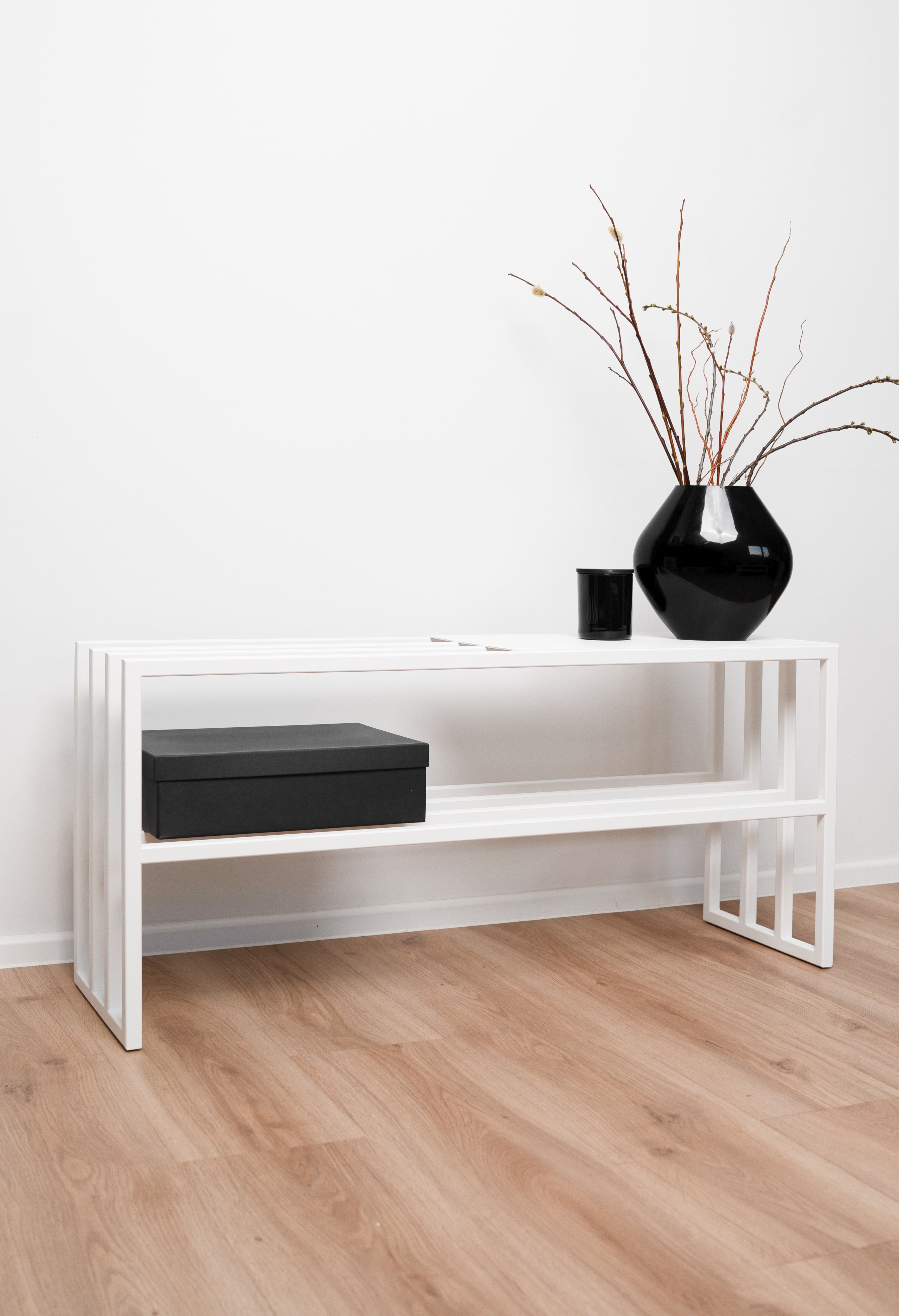 Schuhregal Frontansicht in weiß mit minimalistischer schwarzer Vase mit Ästen dekoriert. Ein schwarzer Karton steht unten im Regal und eine schwarze Kerze oben auf der Sitz und Ablagefläche neben der Vase.