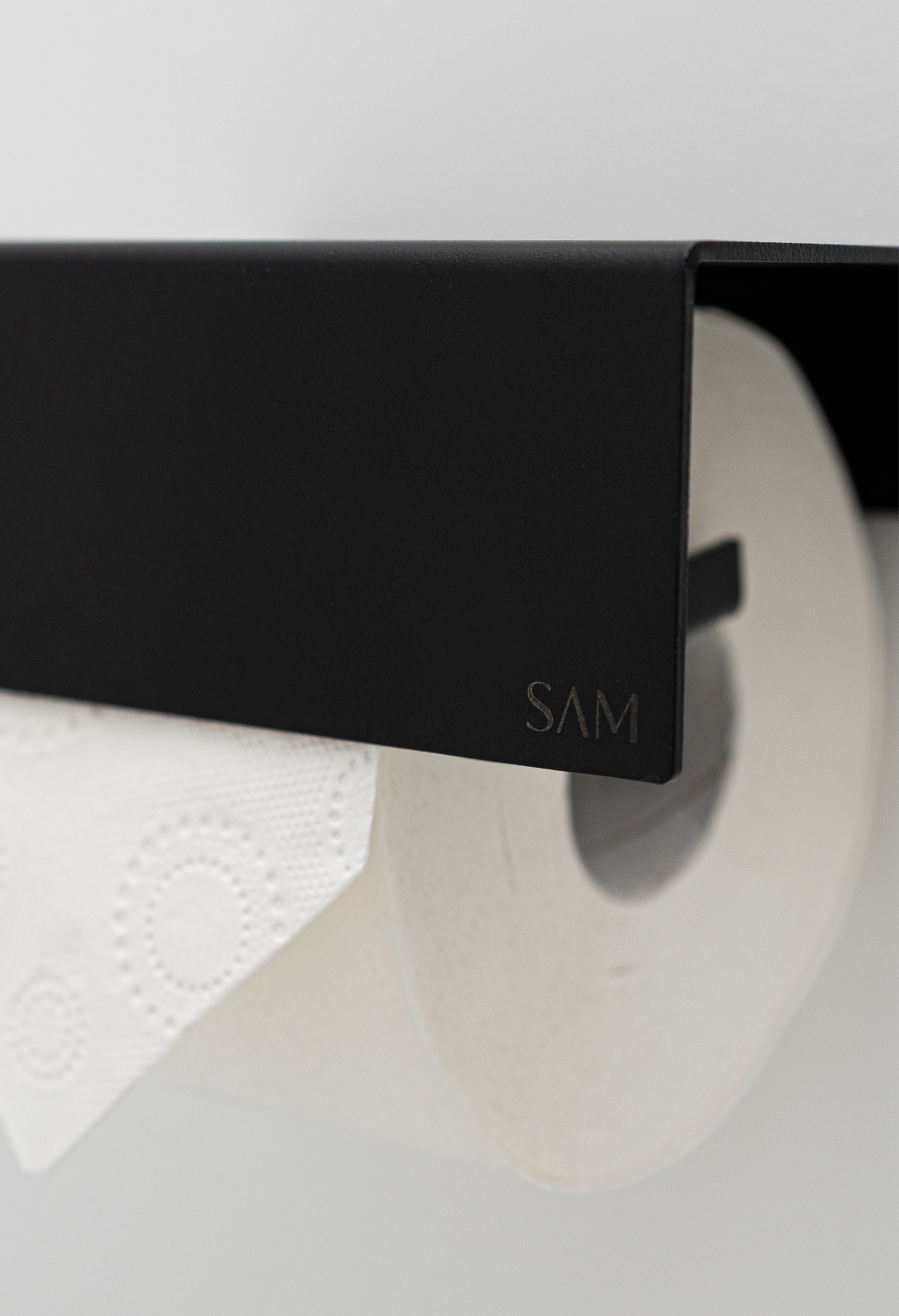 Toilettenpapierhalter LILLE zum Kleben ohne Bohren in Farbe schwarz Close-up Oberflächenbeschaffenheit Pulverbeschichtung und gelasertes SAM Logo.