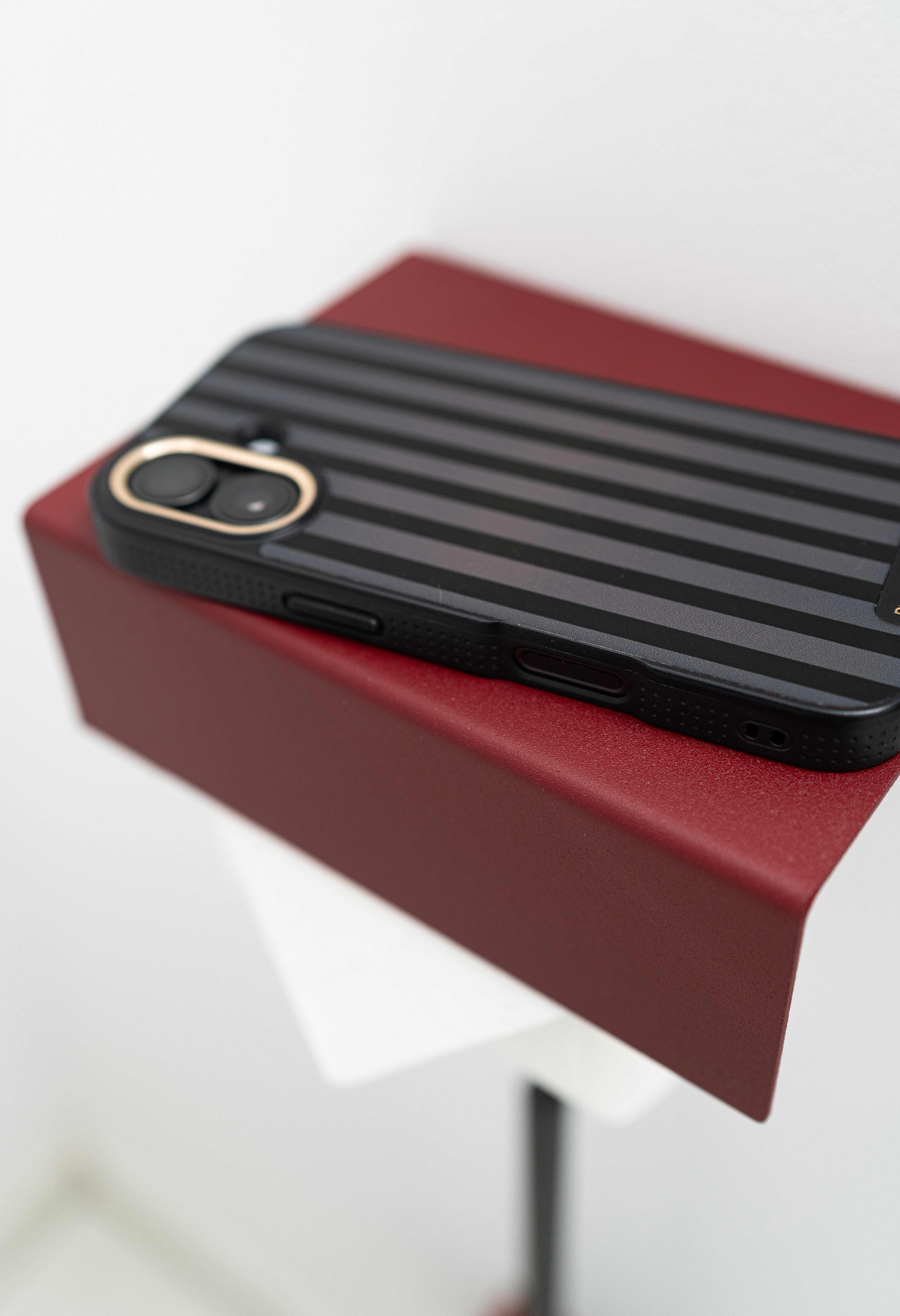 Toilettenpapierhalter LILLE zum Kleben ohne Bohren in Farbe Velvet Red mit Iphone, welches auf der Ablage liegt.