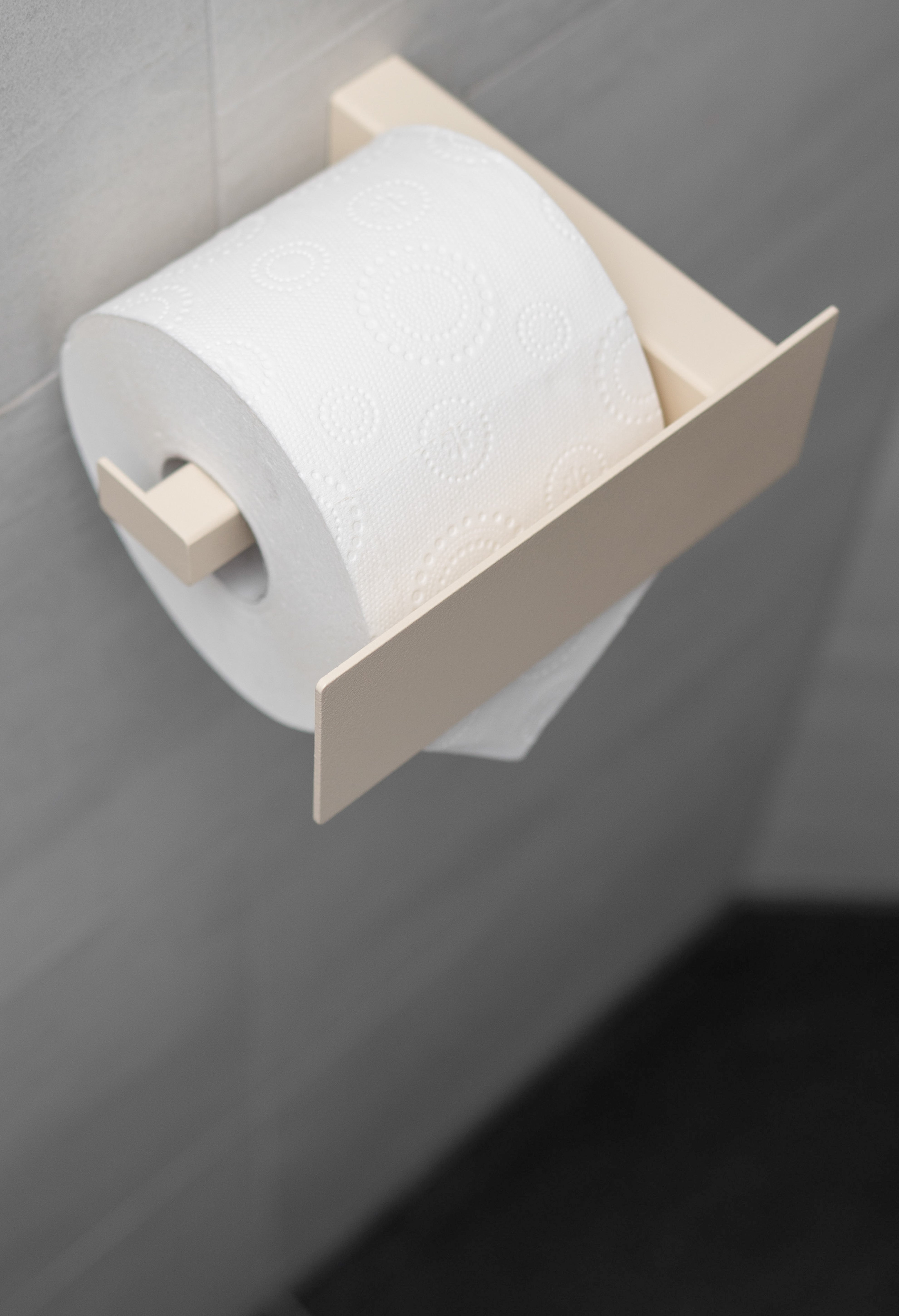 Beiger pulverbeschichteter Toilettenpapierhalter aus Metall mit Blende in schräger Ansicht.