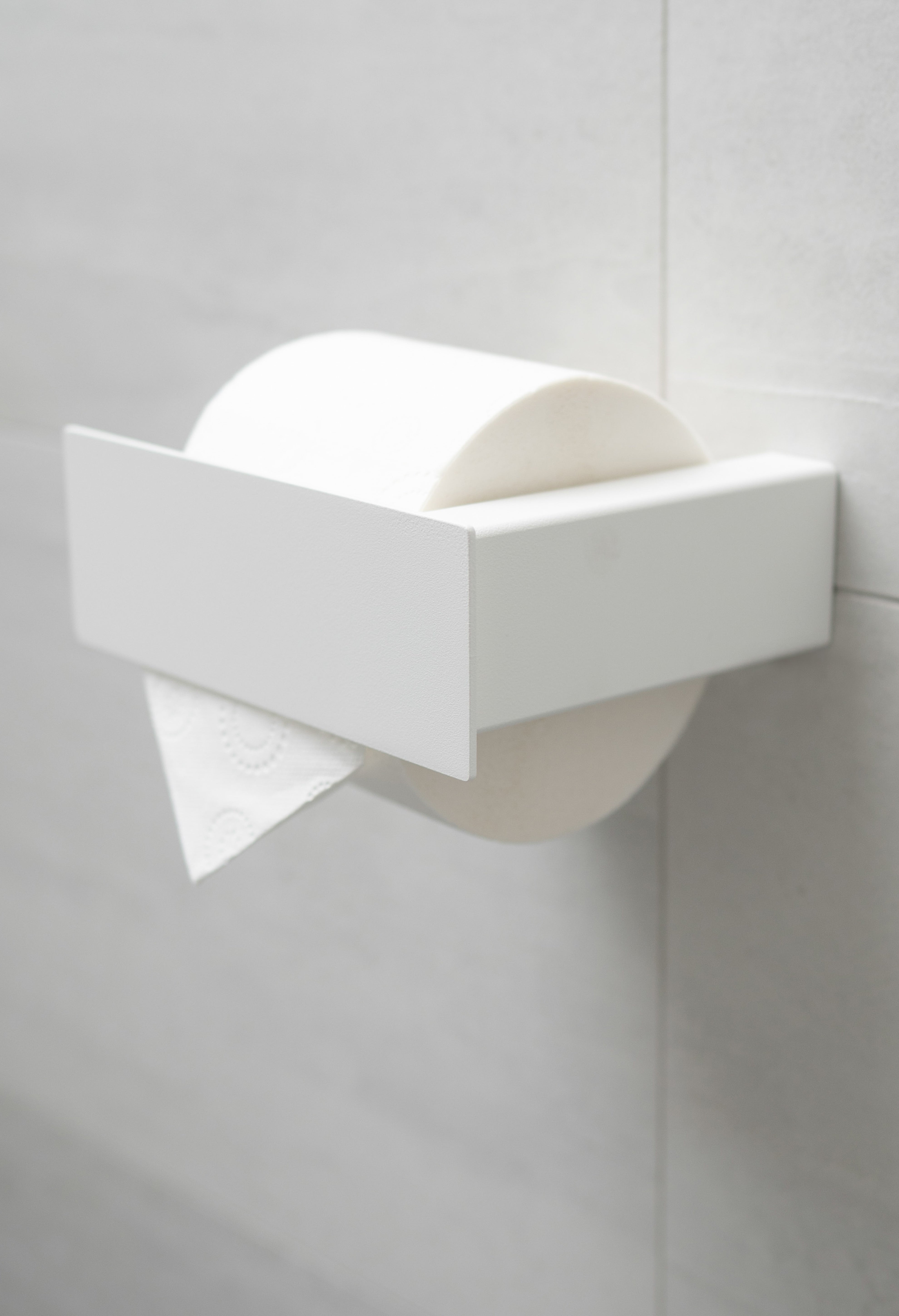 Weisser pulverbeschichteter Toilettenpapierhalter aus Metall mit Blende an weißen Fliesen.