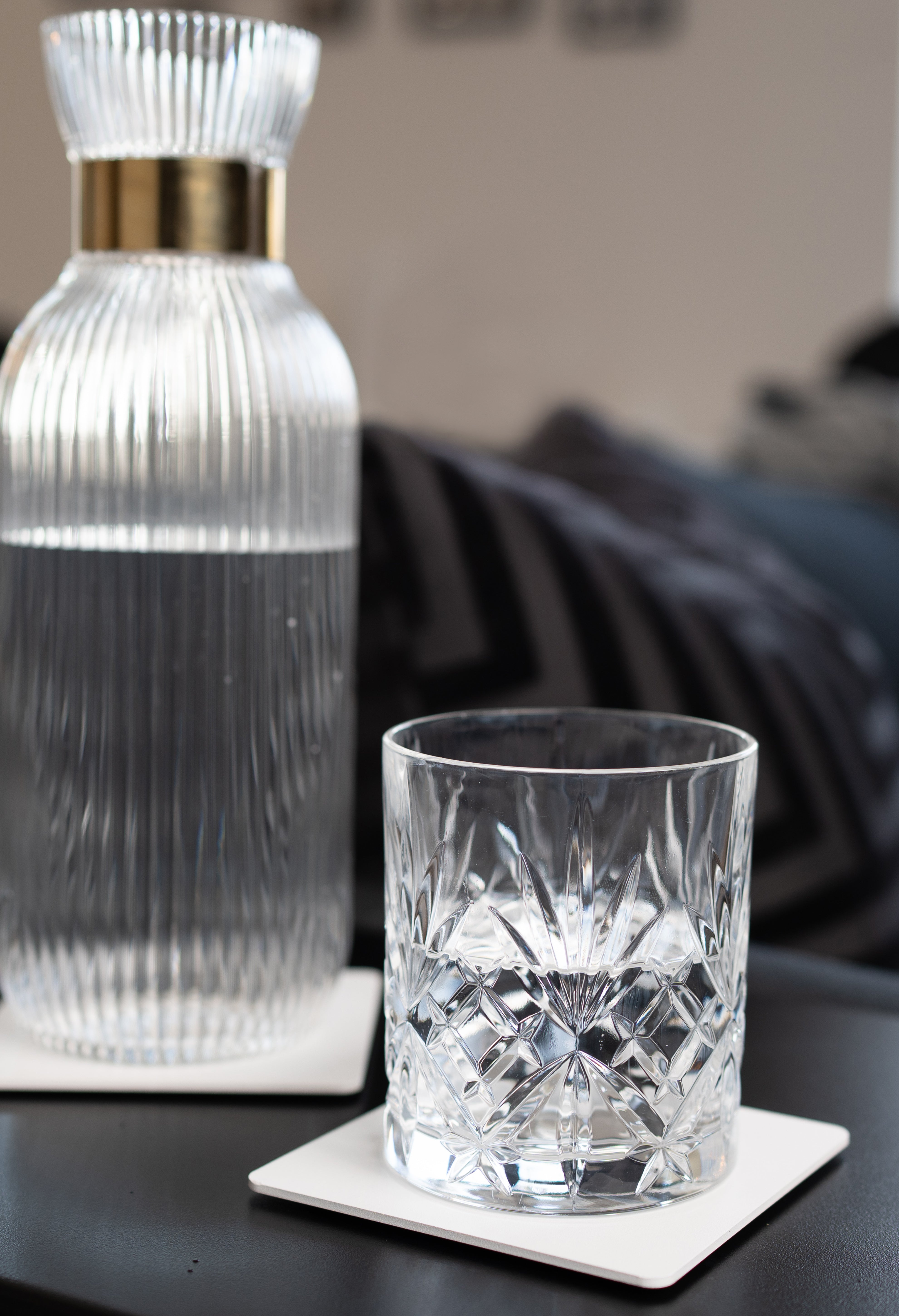 Weisse pulverbeschichtete Metall Untersetzer auf schwarzer Oberfläche mit schönem Kristallglas und geriffelter Glaskaraffe.