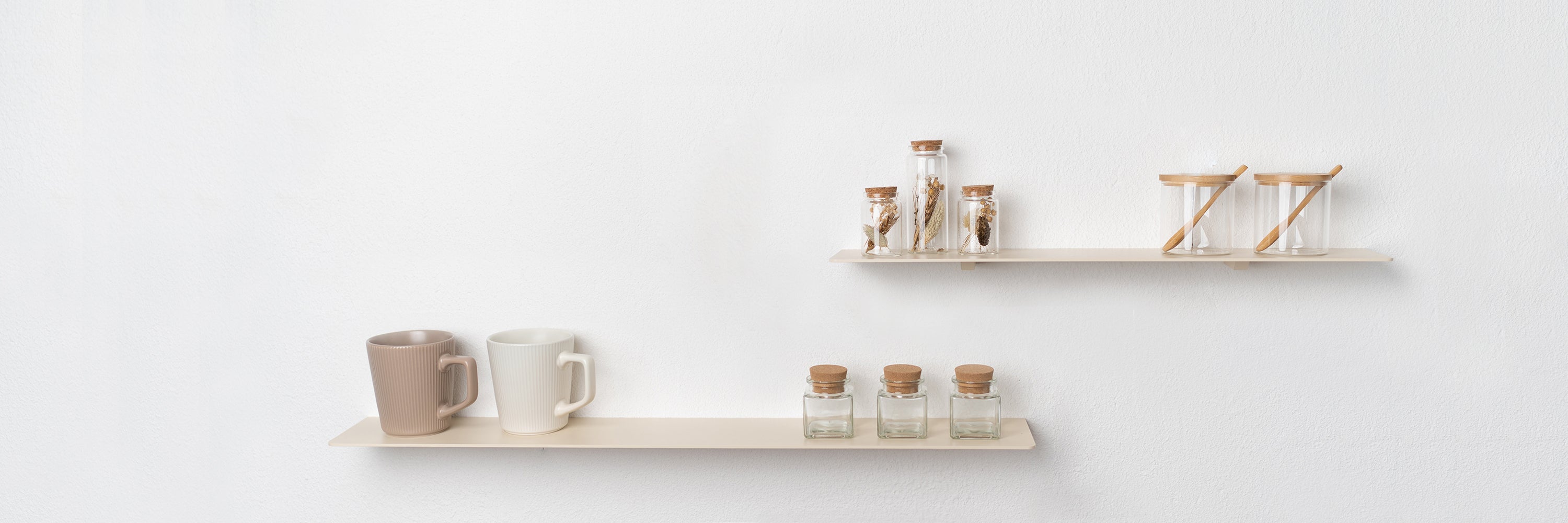 Zwei minimalistische Wandregale aus Metall in einer hellen Küche, dekoriert mit Tassen, Gewürzgläsern und Aufbewahrungsgläsern mit Holzdeckeln und Löffeln. Die Regale sind dezent in neutralem Beige gehalten und bieten stilvollen, funktionalen Stauraum