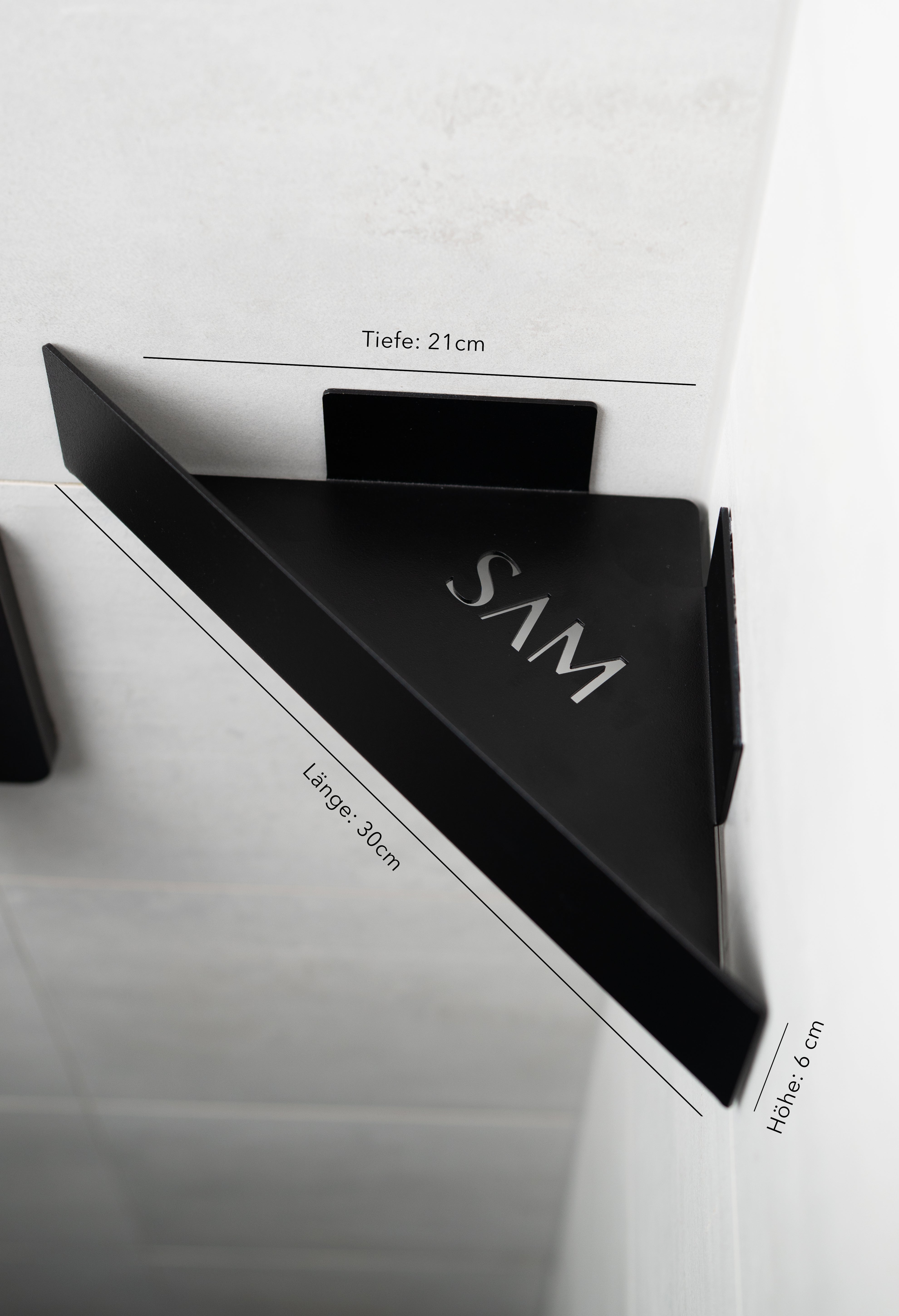 Produktgrafik des minimalistischen Dusch-Eckregals MONTE CARLO aus pulverbeschichtetem Metall in Mattschwarz mit exakten Abmessungen. Das dreieckige Regal ist in einer Fliesenecke montiert, zeigt eine edle, durchbrochene „SAM“-Logo-Prägung auf der Stellfläche und ist mit feinen Maßlinien beschriftet: Länge 30 cm an der Vorderseite, Tiefe 21 cm an den Wandseiten und eine Höhe von 6 cm für die vordere Blende.