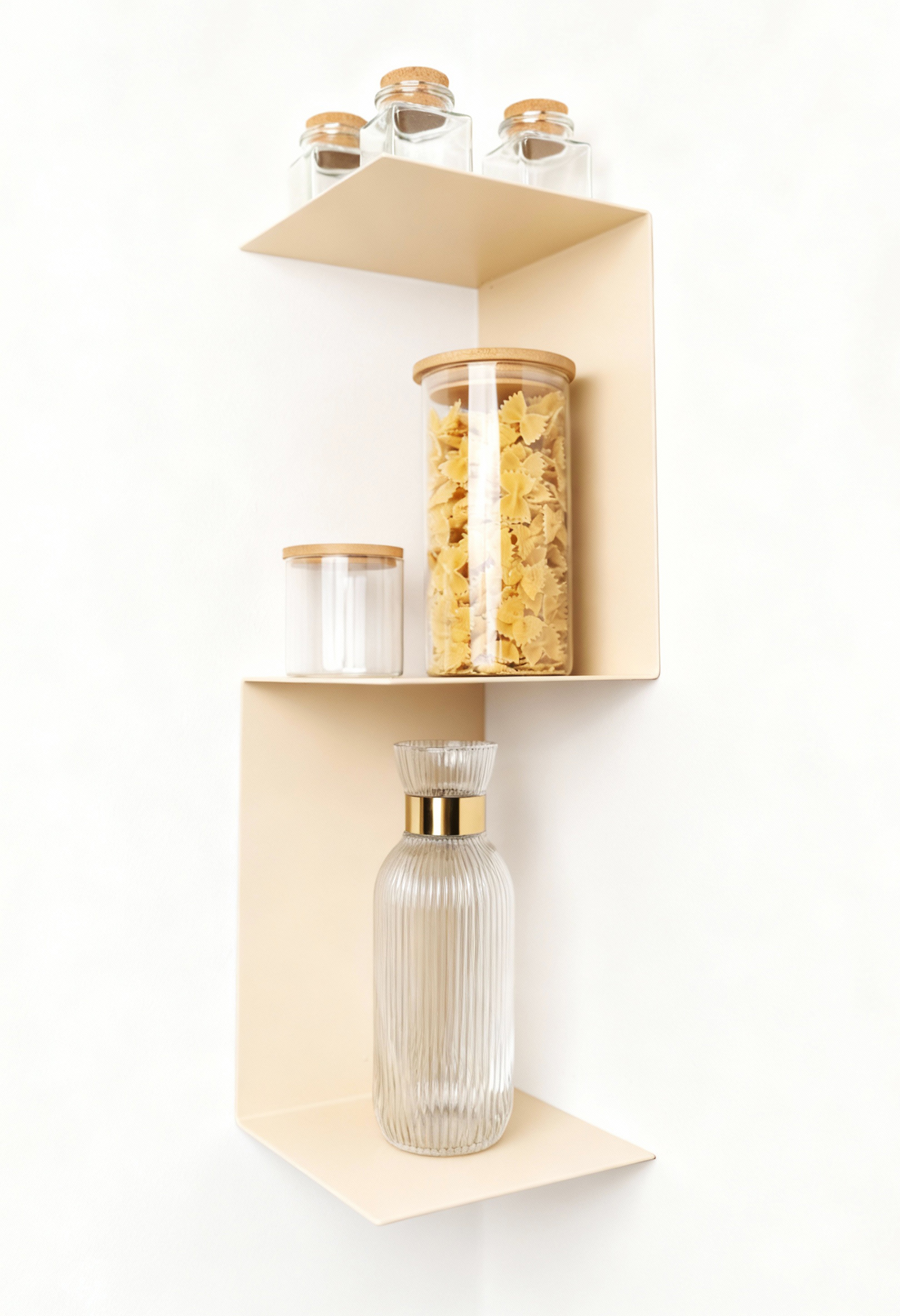 beiges, minimalistisches Eckwandregal aus Metall, das in einer Ecke hängt und mit Glasgefäßen dekoriert ist. Die Gefäße enthalten Nudeln und Gewürze, eines der Gläser hat einen Holzdeckel. Das Regal bietet eine stilvolle und platzsparende Lösung für die Raumnutzung in der Küche