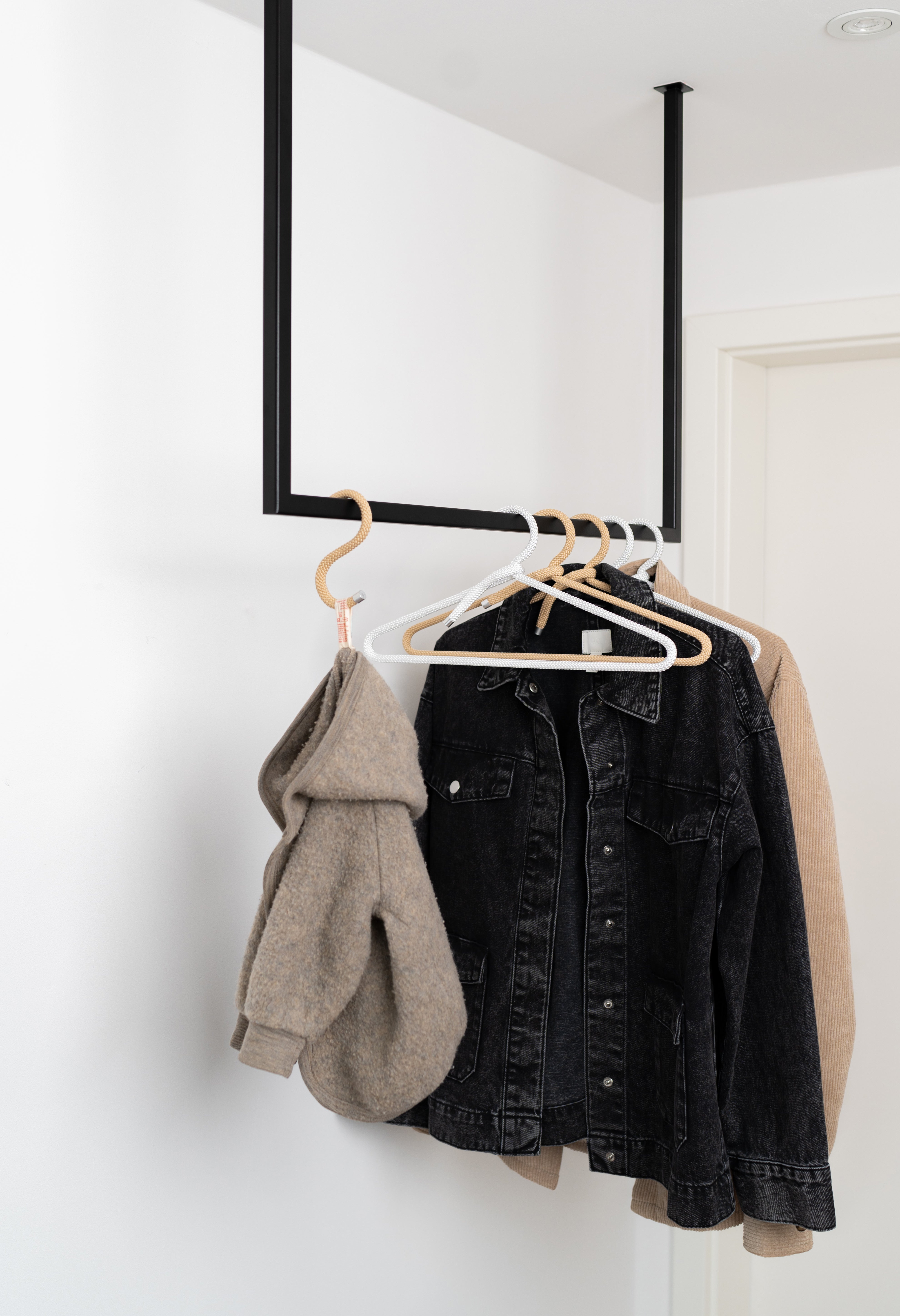 Schwarze Metallgarderobe in U-Form mit beigen und weißen Kleiderbügeln, zwei Jacken und einer Kinderjacke an einem S-Haken.