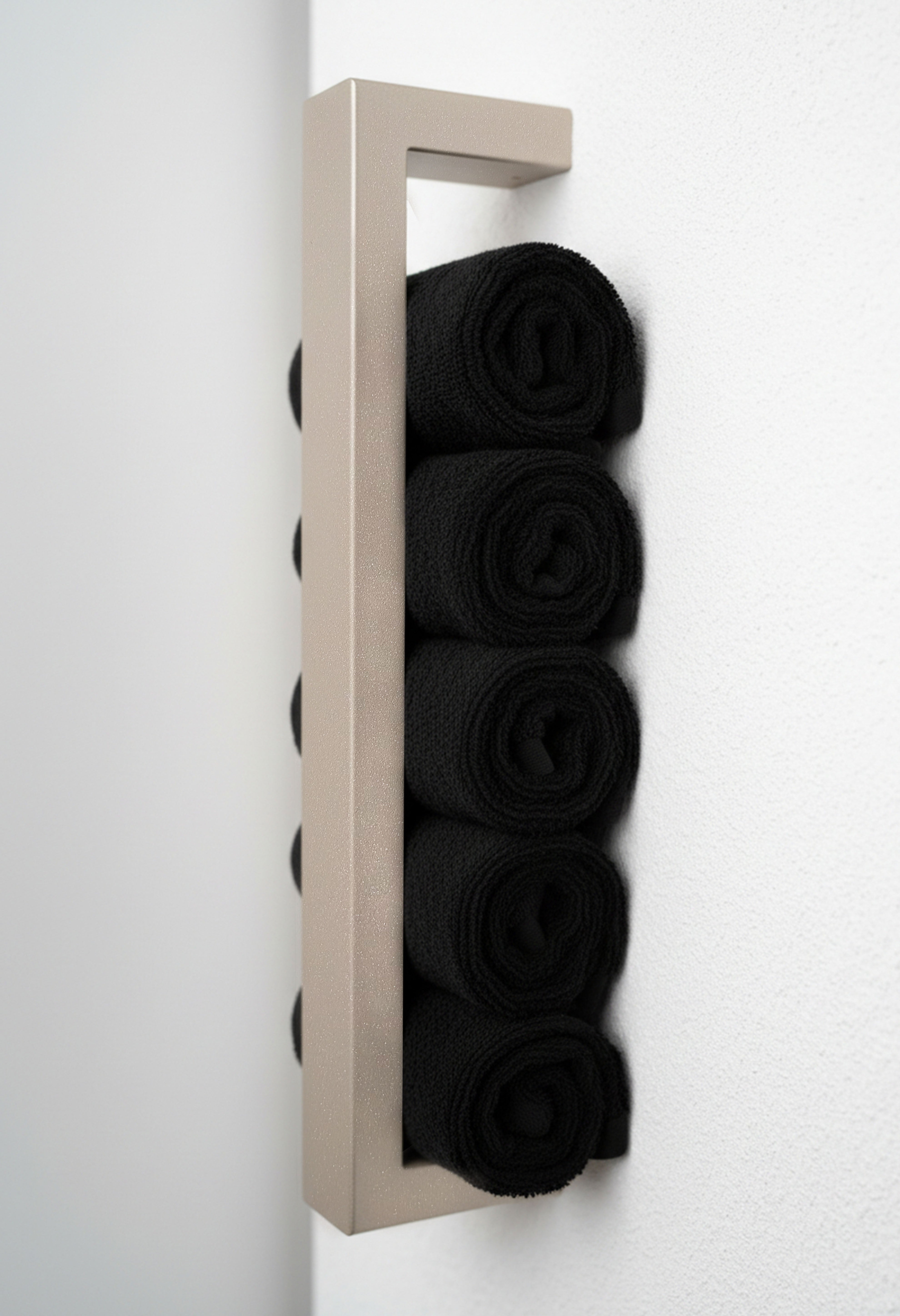Champagner farbener, moderner Handtuchhalter aus pulverbeschichtetem Metall, der an einer Wand montiert ist. Der Halter bietet Platz für mehrere gerollte Handtücher und fügt sich dekorativ in das Badezimmer ein. Eine stilvolle, platzsparende Lösung zur Aufbewahrung von Handtüchern.