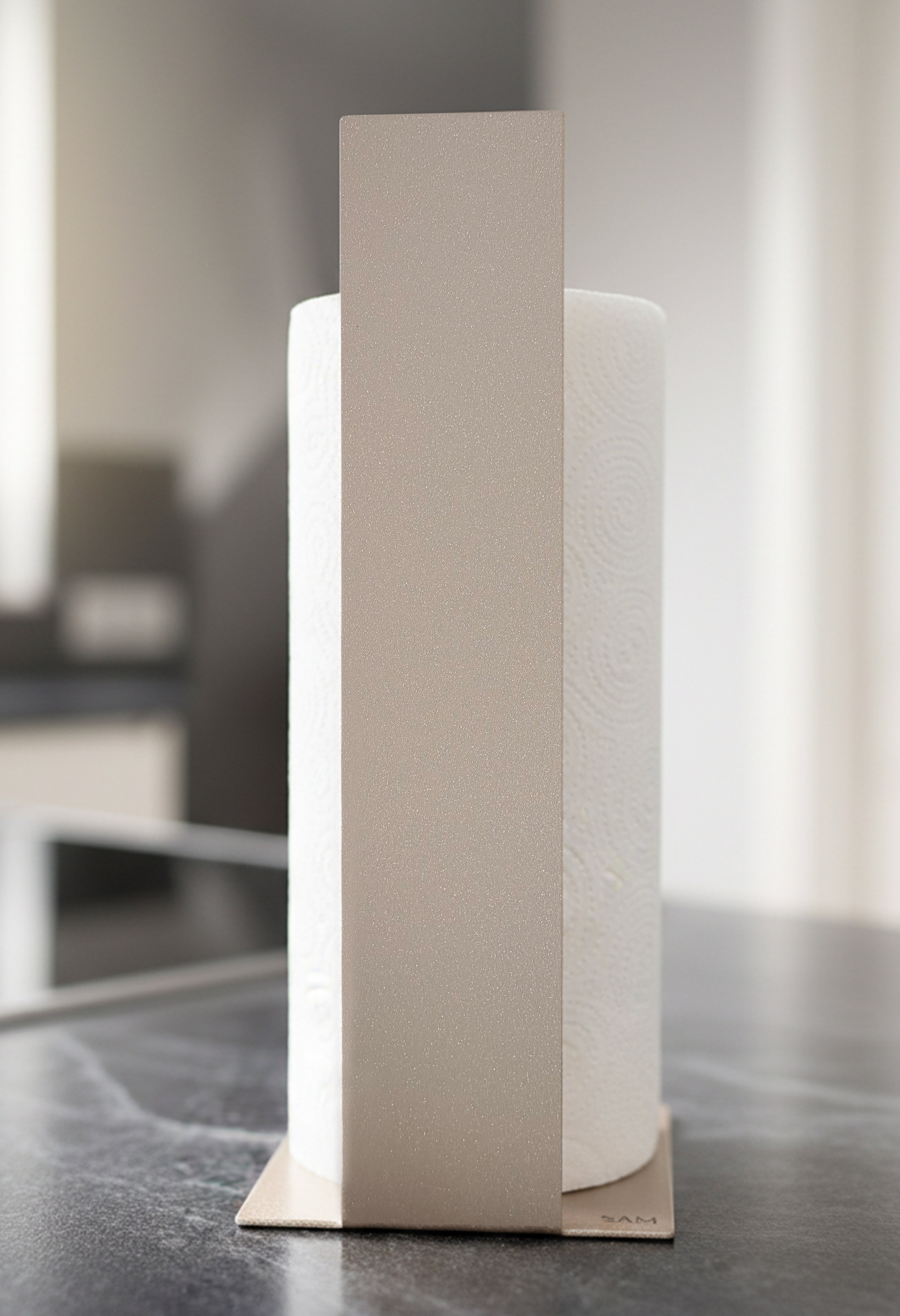 Küchenrollenhalter Granada pulverbeschichtet in Champagner, glitzernd, metallic, auf einer dunklen Marmorarbeitsfläche in einer hellen Küche. Frontansicht.