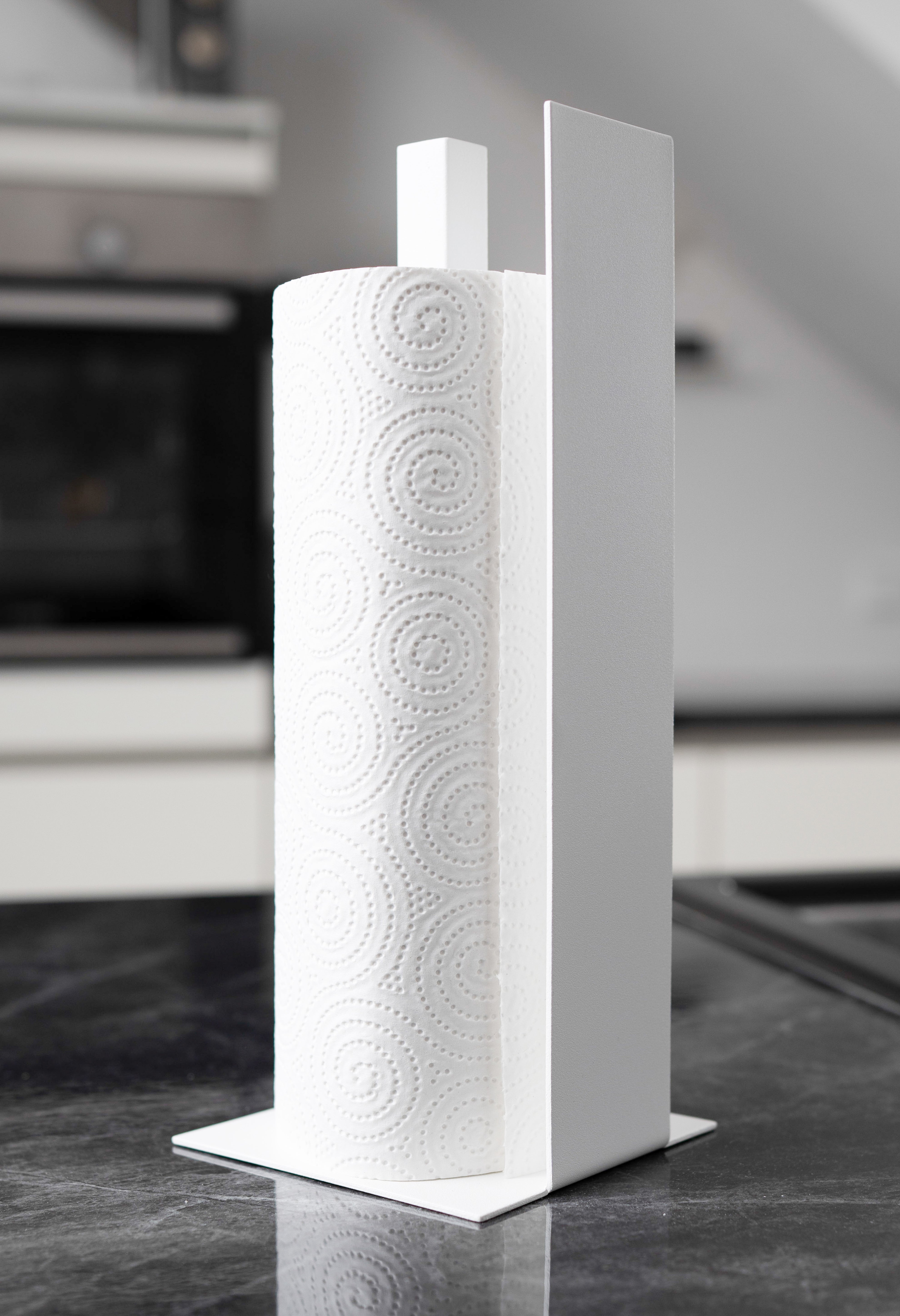 Küchenrollenhalter Granada pulverbeschichtet in matt weiss auf einer dunklen Marmorarbeitsfläche in einer hellen Küche. Schräge Ansicht von vorne.