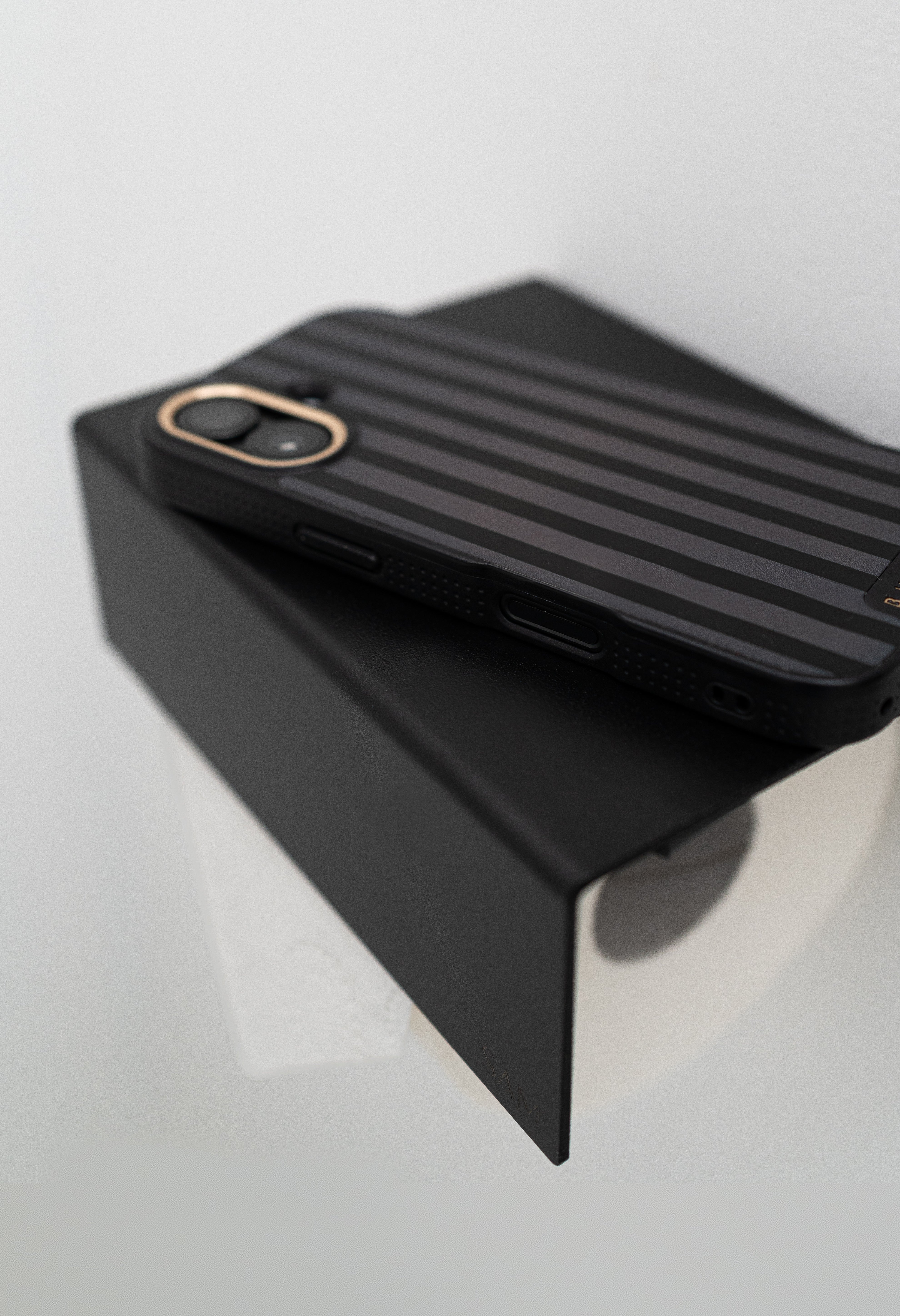 Toilettenpapierhalter LILLE zum Kleben ohne Bohren in Farbe schwarz mit Iphone, welches auf der Ablage liegt.