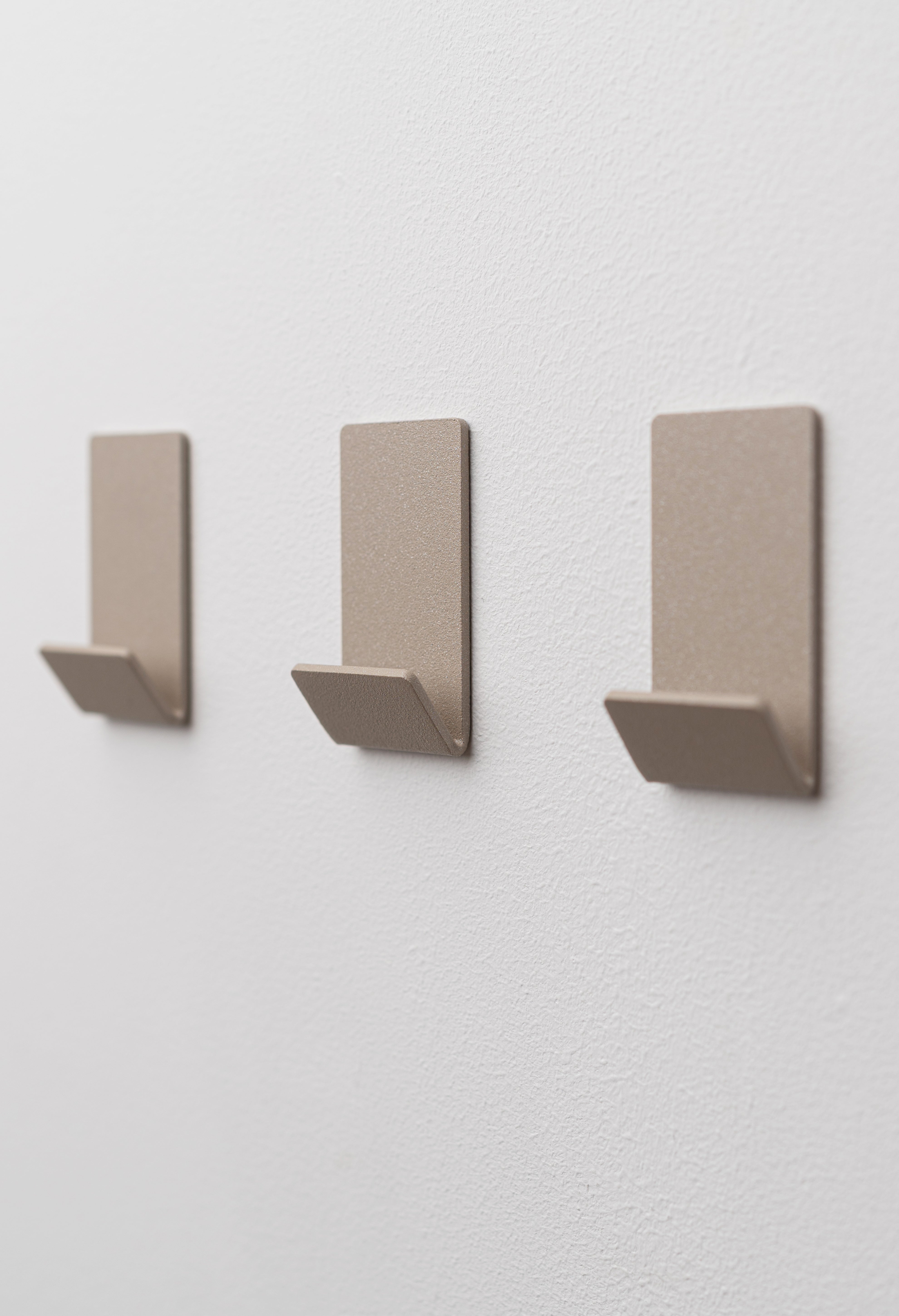 Wandhaken zum Kleben Ohne Bohren in Champagner pulverbeschichtet als dreier Set an weißer Wand.