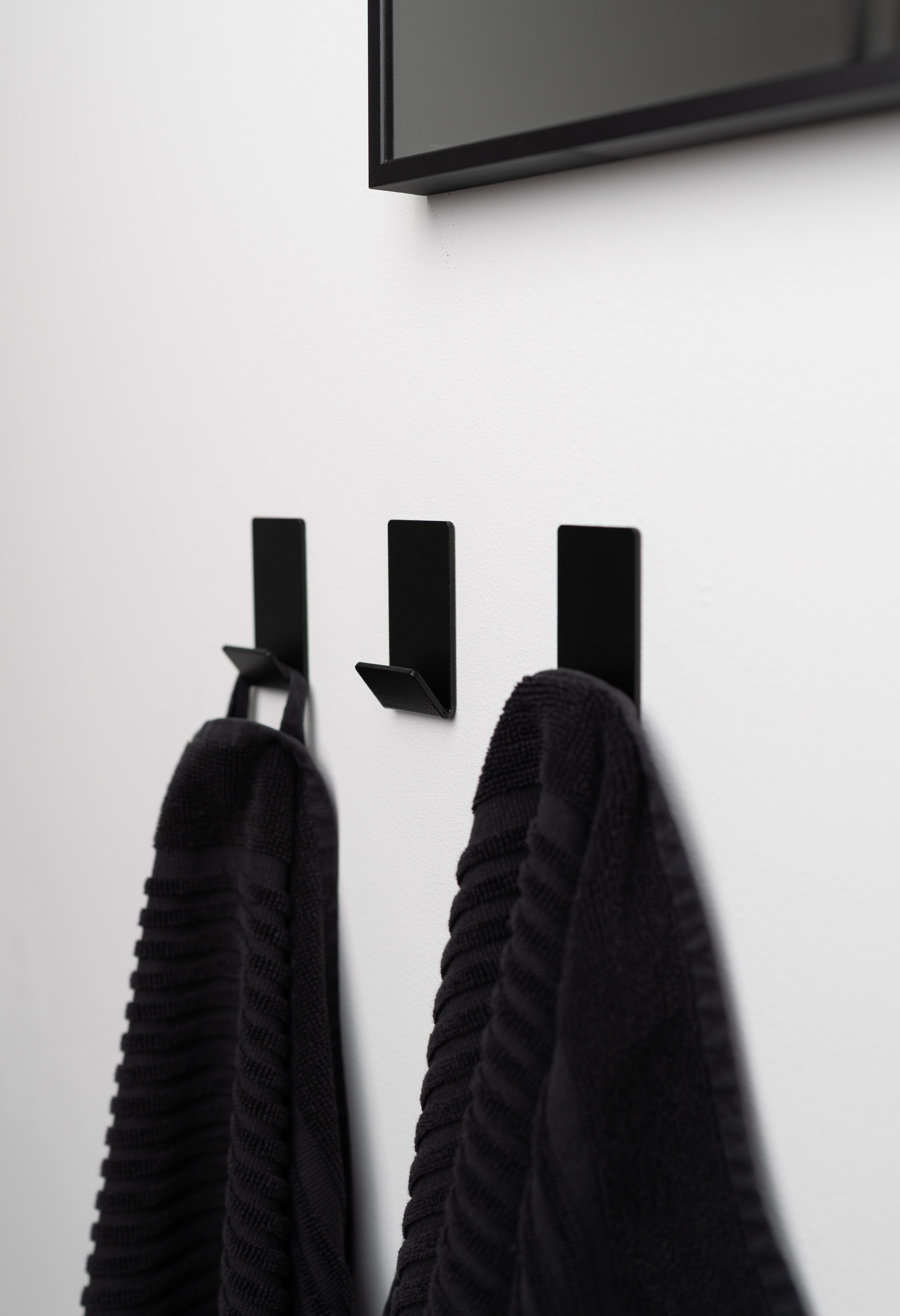 Wandhaken zum Kleben Ohne Bohren in schwarz pulverbeschichtet als dreier Set an weißer Wand mit schwarzen Handtüchern