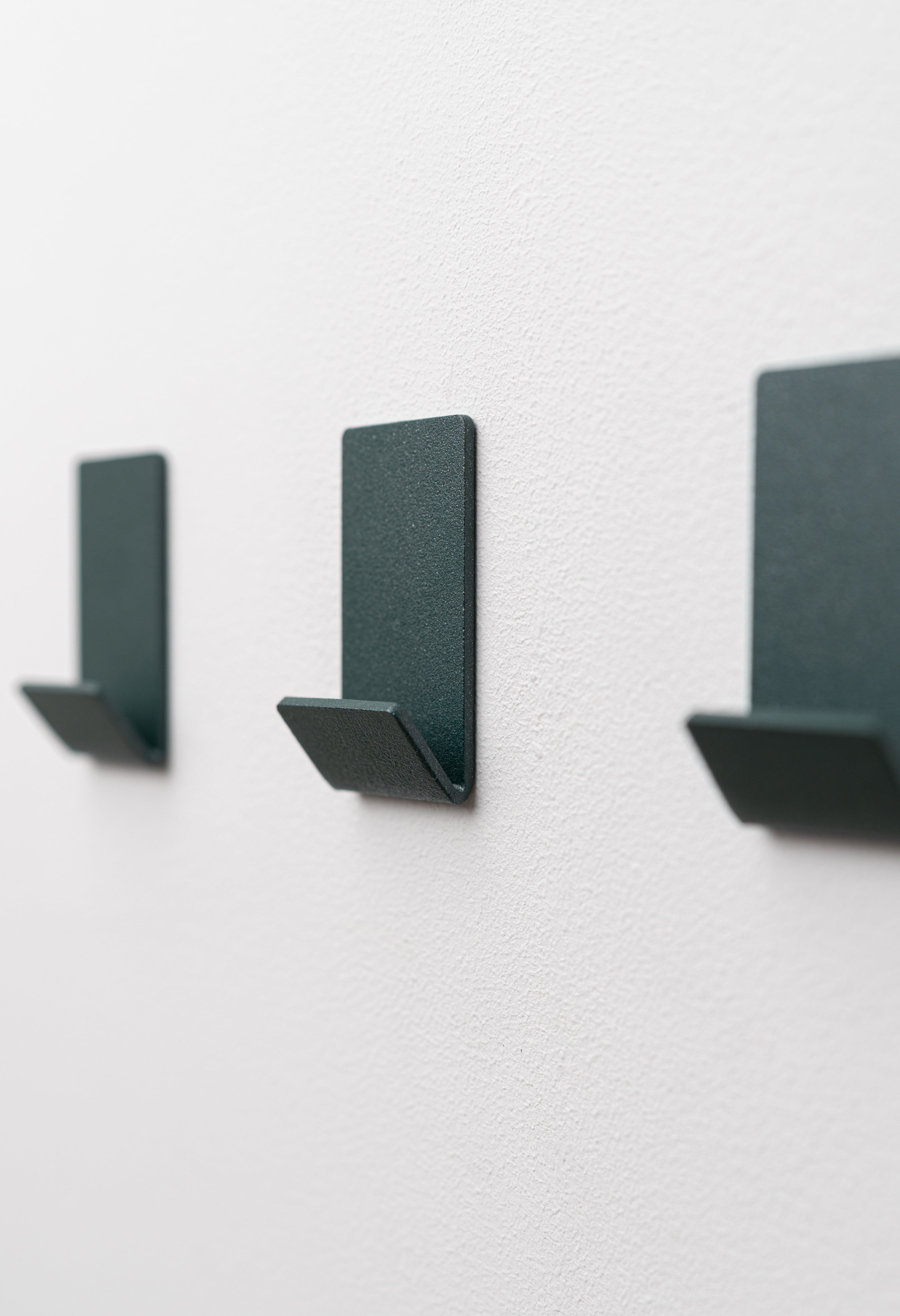 Wandhaken zum Kleben Ohne Bohren in Sparkling Green pulverbeschichtet als dreier Set an weißer Wand.